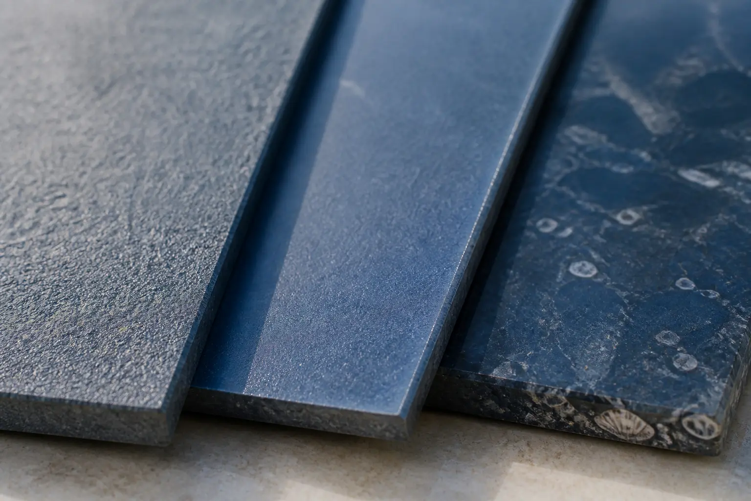 Trois finitions de pierre bleu côte à côte : brut sablé, brossé et poli humide, avec textures visibles.