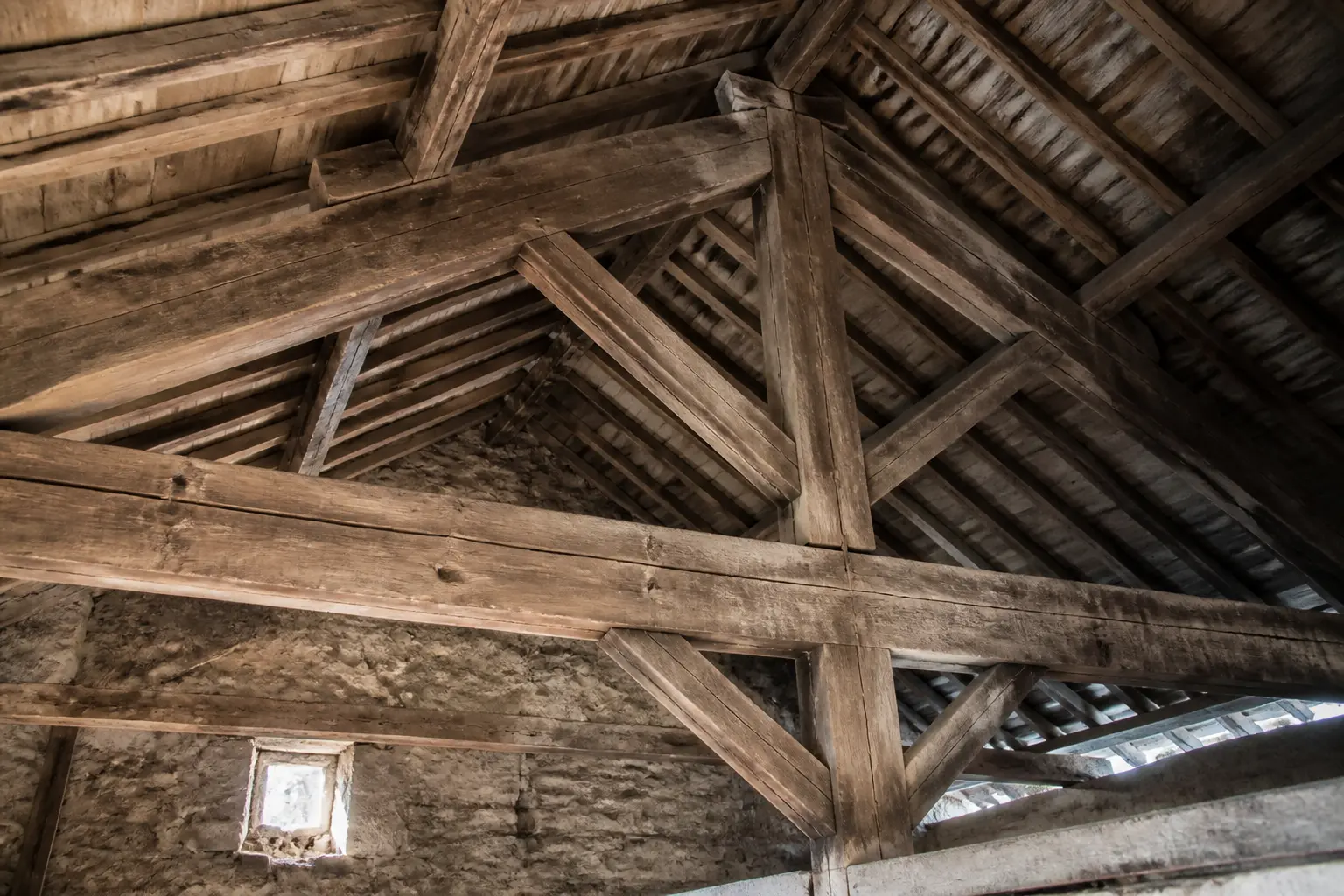Charpente bois traitement : vieille charpente d’atelier avec poutres apparentes, fissures légères et poussière visible.