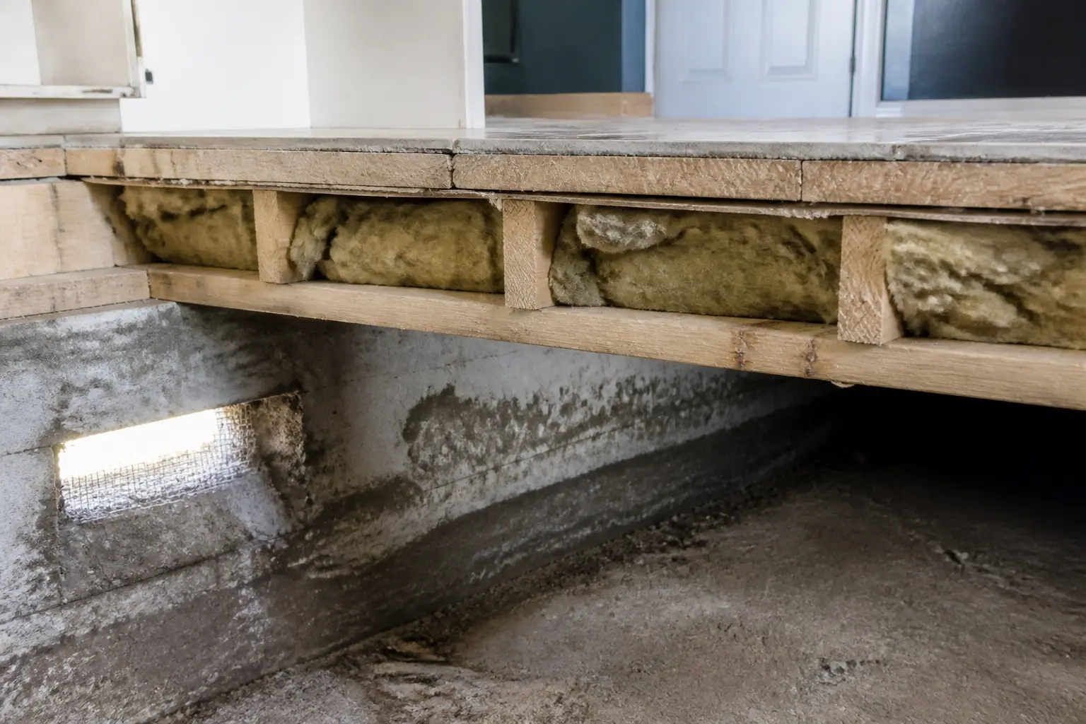 Isolation plancher bas : sous-sol humide avec solives apparentes, laine minérale posée et traces de déperdition thermique.