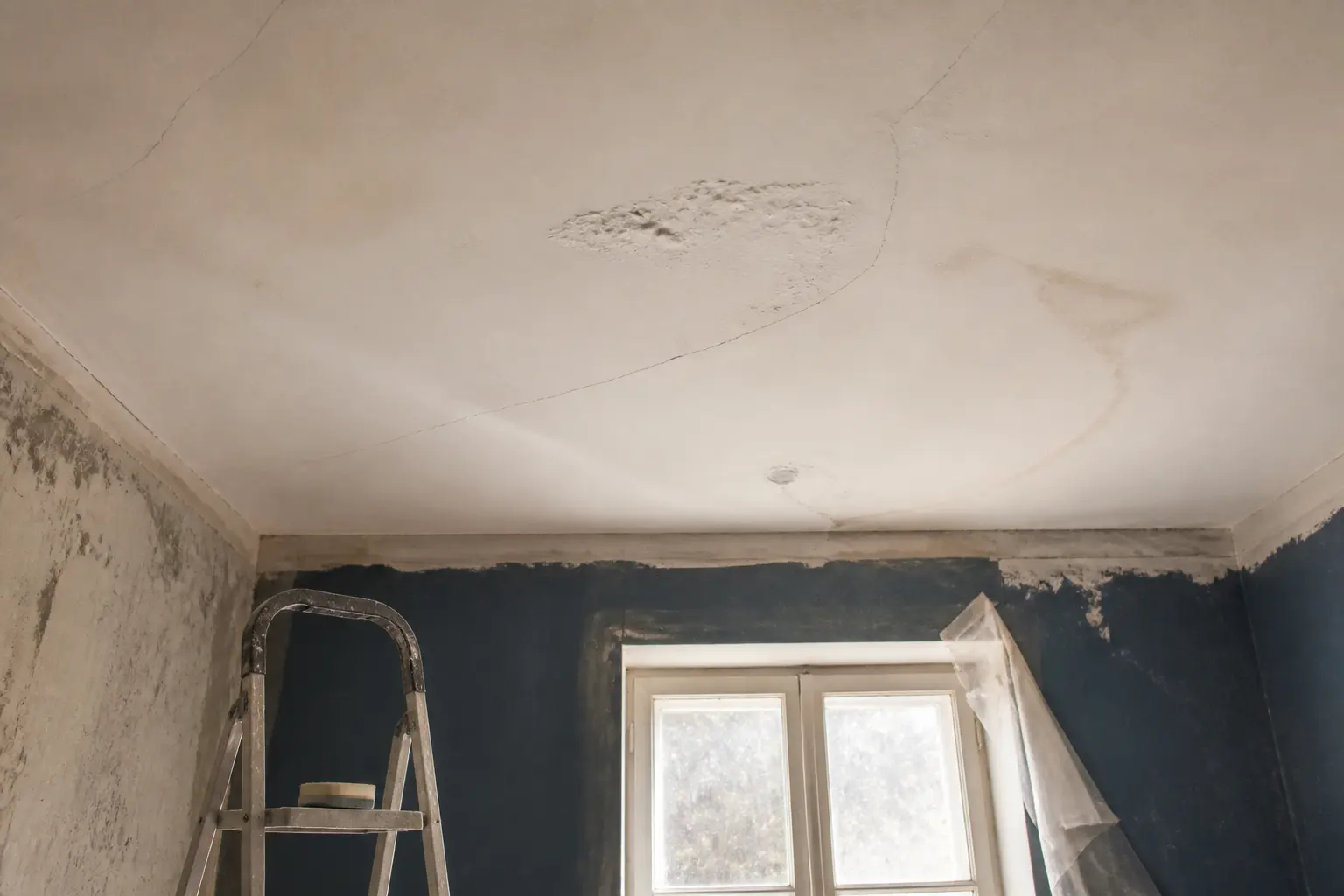 Avant de peindre un plafond, inspection d’un plafond fissuré avec tache d’humidité, escabeau et bâche au sol