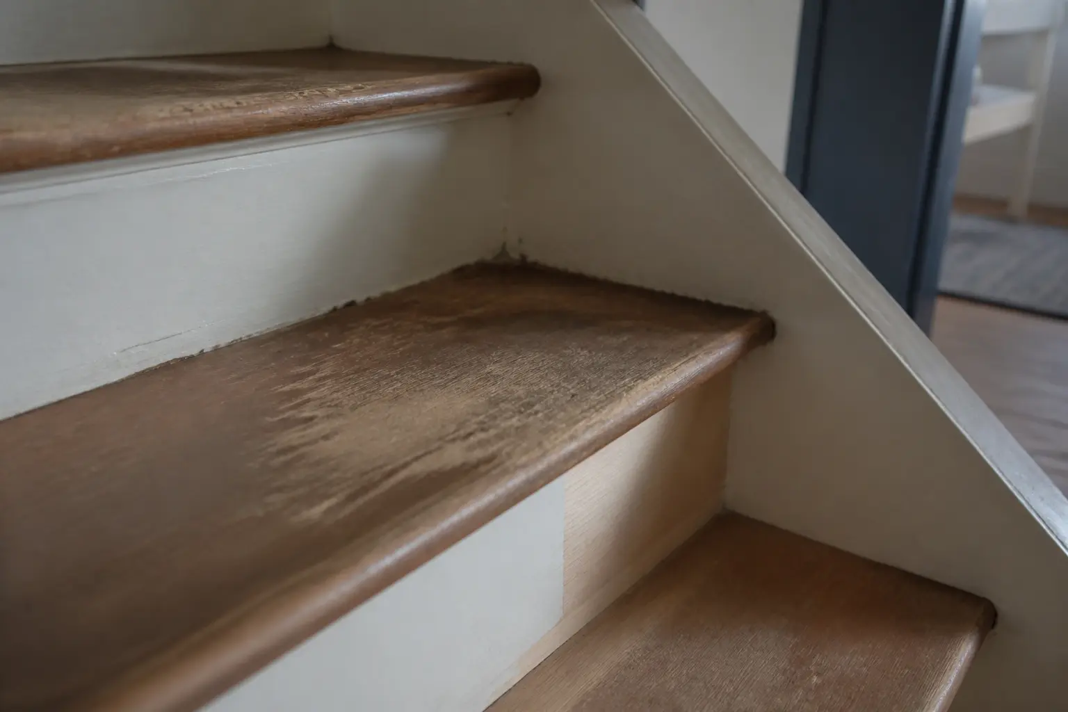 Peinture bois escalier : escalier en bois usé, marche rayée et riser légèrement écaillé, lumière naturelle douce.