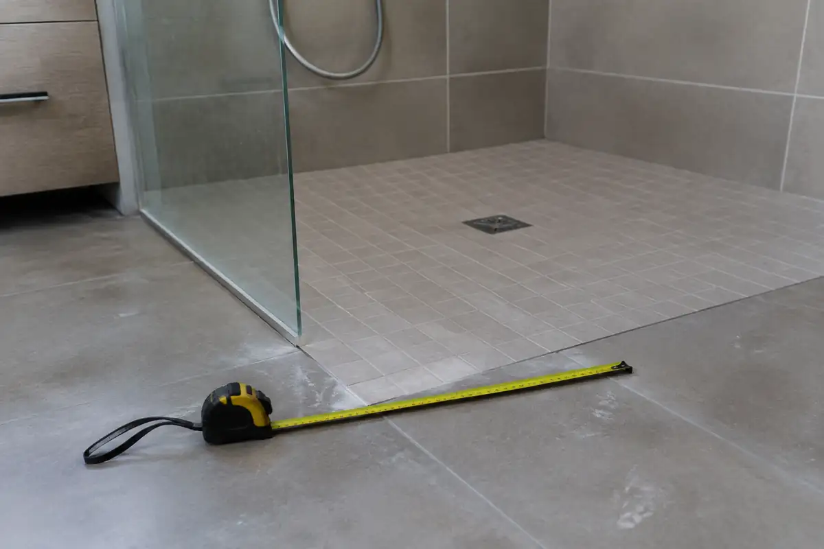 Mètre ruban posé sur un sol carrelé devant une douche de plain-pied